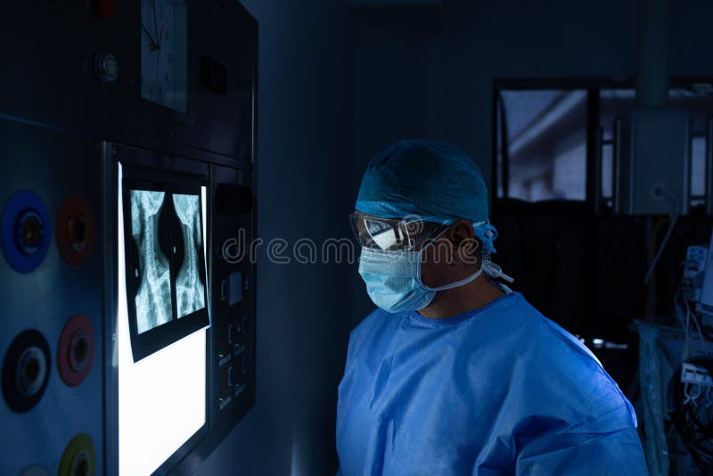 Cirujano de sexo masculino que lee el rayo de x en sala de operaciones en el hospital fotos de archivo libres de regalías Cirujano de sexo masculino que lee el rayo de x en sala de operaciones en el hospital fotos de archivo libres de regalías