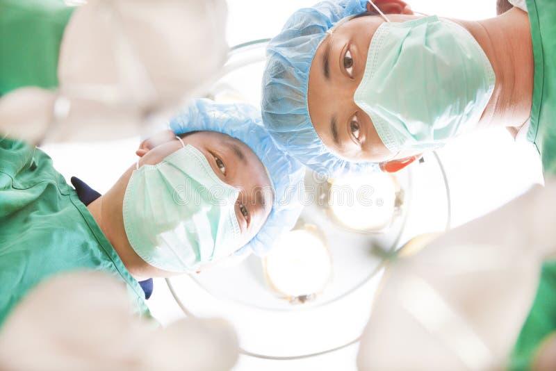 Cirurgiões e assistente médico que trabalham na sala de operações fotografia de stock Cirurgiões e assistente médico que trabalham na sala de operações fotografia de stock