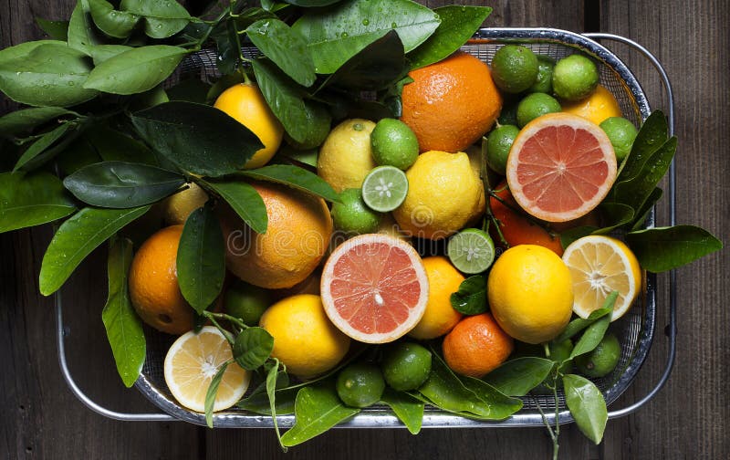 Citrus fruit including meyer lemons, key limes, persian limes, grapefruit and oranges freshly washed in stainless steel basket with wood background.