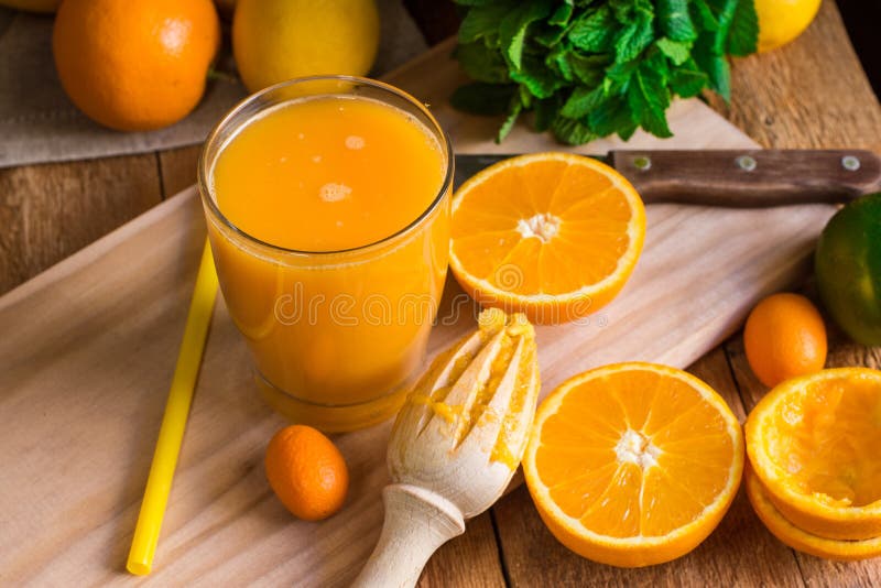 Citrus fruits oranges lemons lime cumquat, fresh mint, reamer, freshly pressed juice in glass on wood kitchen table by window, top view. Citrus fruits oranges lemons lime cumquat, fresh mint, reamer, freshly pressed juice in glass on wood kitchen table by window, top view