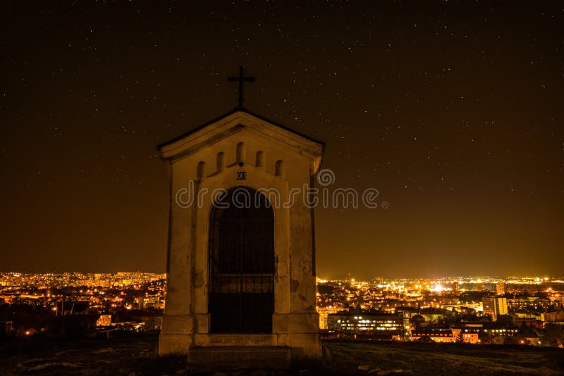 Mestská noc v Nitre z vyhliadky na vrchole kopca Slovenské mesto Nitra s jasnou nočnou oblohou a krížmi. Centrum mesta