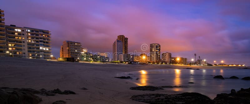 City skyline of Povoa de Varzim, Portugal at night from beach, with light reflections on the ocean.