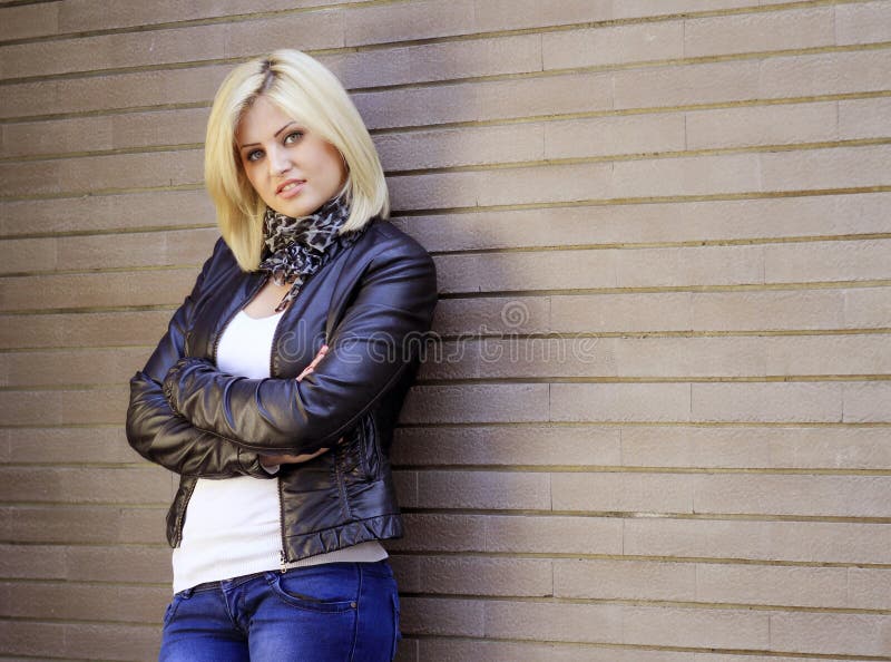 City woman dressed in casual urban outfit - jeans and leather jacket, posing next to a brick wall, half body