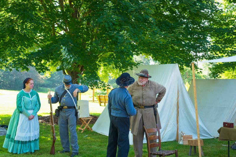 TWINSBURG, OH - JUNE 30, 2018: A group of Civil War reenactors converse by tents and displays in the shade during an all-day history event at the Twinsburg Public Library. TWINSBURG, OH - JUNE 30, 2018: A group of Civil War reenactors converse by tents and displays in the shade during an all-day history event at the Twinsburg Public Library.