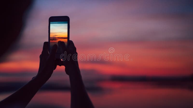 Ciérrese encima de las manos con la imagen del smartphine de la hembra que hace una puesta del sol increíble el tiro rápido fotografía de archivo libre de regalías Ciérrese encima de las manos con la imagen del smartphine de la hembra que hace una puesta del sol increíble el tiro rápido fotografía de archivo libre de regalías