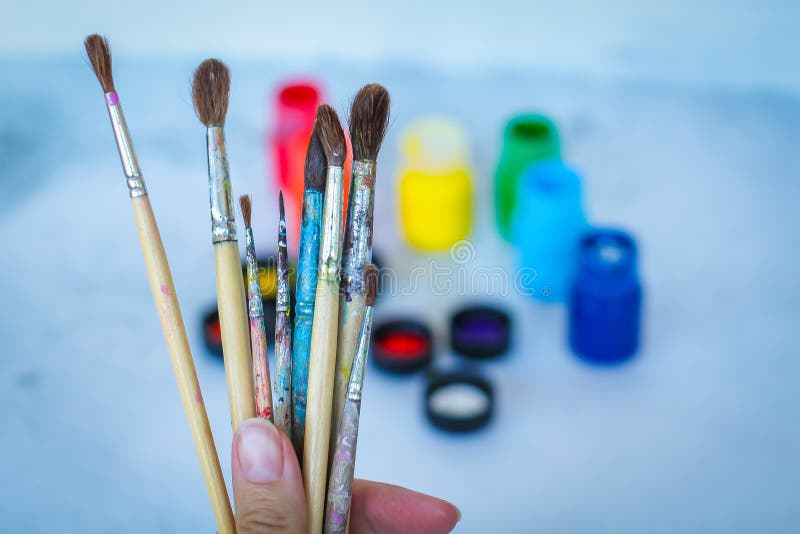 Ciérrese encima de vista de la mano femenina con el sistema de brochas en fondo borroso azul con las latas de las pinturas fotografía de archivo libre de regalías Ciérrese encima de vista de la mano femenina con el sistema de brochas en fondo borroso azul con las latas de las pinturas fotografía de archivo libre de regalías