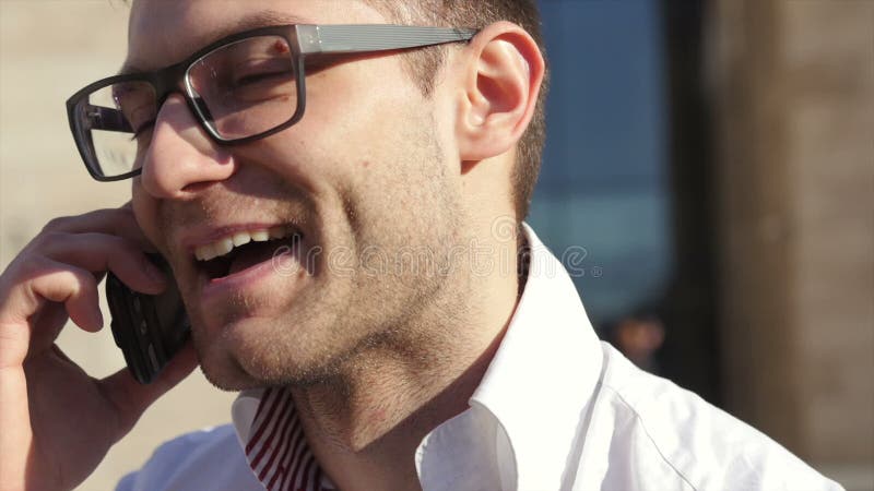 Ciérrese encima del retrato del hombre de negocios masculino en el teléfono elegante al aire libre en la camisa blanca