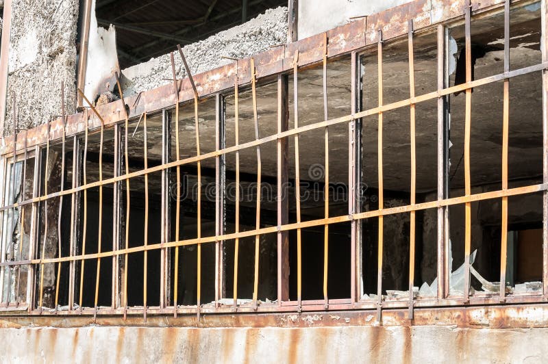 Ciérrese para arriba de barras de seguridad del metal en las ventanas de las paredes dañadas de la pequeña casa con los agujeros foto de archivo Ciérrese para arriba de barras de seguridad del metal en las ventanas de las paredes dañadas de la pequeña casa con los agujeros foto de archivo