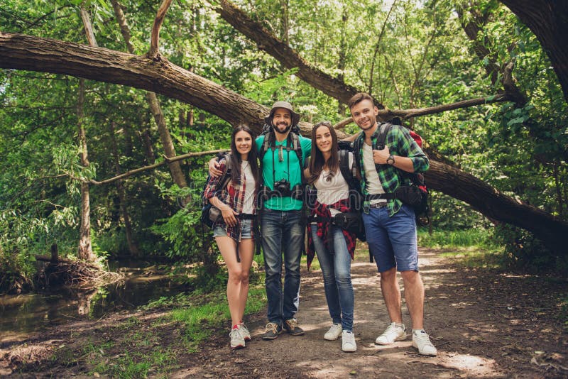 Ciérrese para arriba de cuatro amigos alegres en la madera agradable del verano Son caminantes, caminando y escogiendo el lugar p foto de archivo libre de regalías Ciérrese para arriba de cuatro amigos alegres en la madera agradable del verano Son caminantes, caminando y escogiendo el lugar p foto de archivo libre de regalías