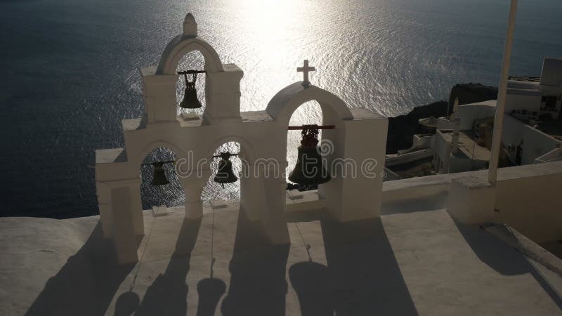 Ciérrese para arriba de cuatro campanas de iglesia en la puesta del sol en Oia, santorini