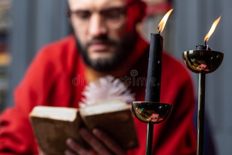 Ciérrese para arriba de dos velas que se colocan en la tabla cerca del libro de lectura del adivino imágenes de archivo libres de regalías Ciérrese para arriba de dos velas que se colocan en la tabla cerca del libro de lectura del adivino imágenes de archivo libres de regalías