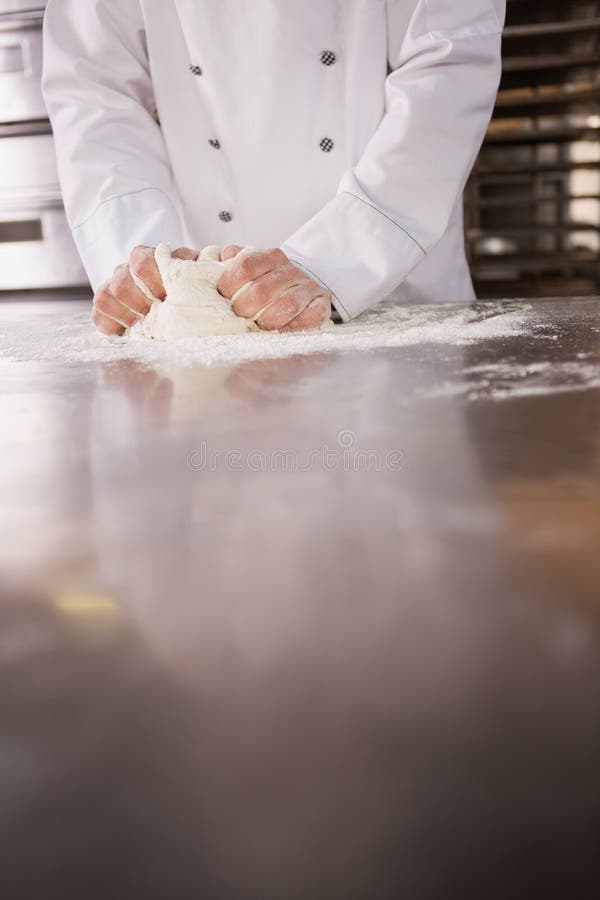 Close up of baker kneading dough on counter in the kitchen of the bakery. Close up of baker kneading dough on counter in the kitchen of the bakery