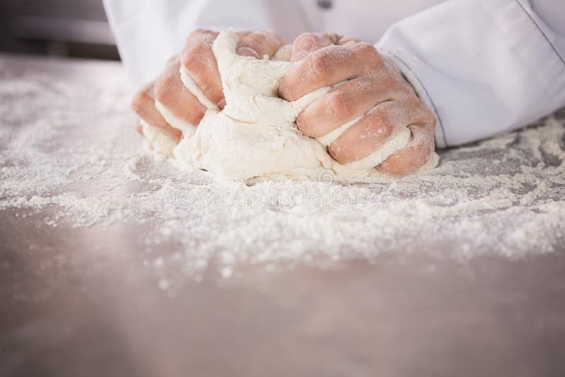 Close up of baker kneading dough on counter in the kitchen of the bakery. Close up of baker kneading dough on counter in the kitchen of the bakery