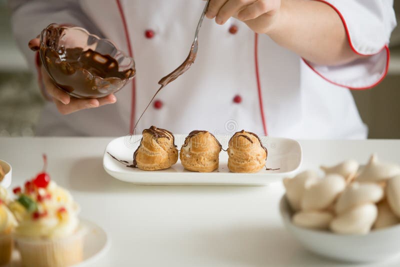 Ciérrese para arriba de las manos profesionales del confitero que esmaltan profiteroles imagen de archivo Ciérrese para arriba de las manos profesionales del confitero que esmaltan profiteroles imagen de archivo