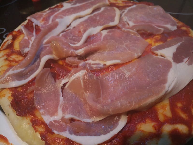 Ciérrese para arriba de tiras de tocino crudas en una pizza cruda imagen de archivo Ciérrese para arriba de tiras de tocino crudas en una pizza cruda imagen de archivo