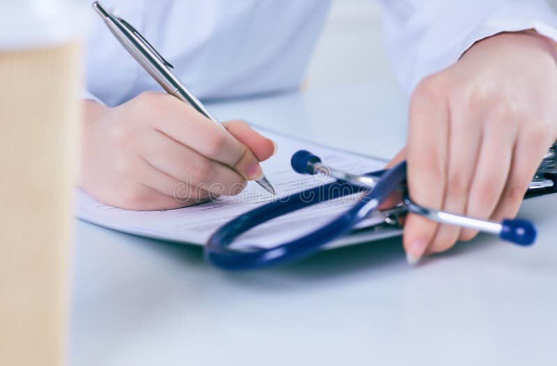 Ciérrese para arriba de un doctor de sexo femenino que llena encima de un formulario de inscripción mientras que consulta al paci fotografía de archivo Ciérrese para arriba de un doctor de sexo femenino que llena encima de un formulario de inscripción mientras que consulta al paci fotografía de archivo