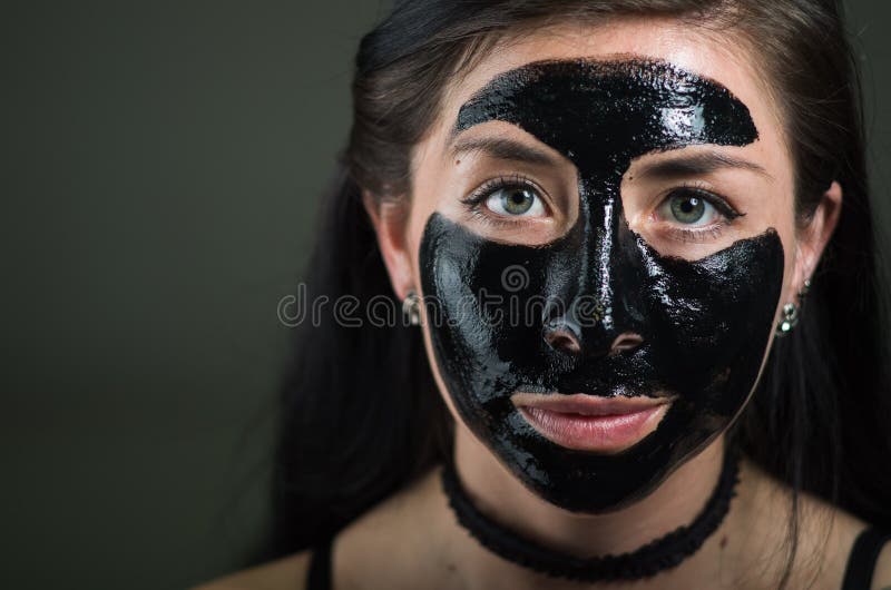 Ciérrese para arriba de una mujer joven de la belleza que usa una máscara negra para limpiar la piel fotos de archivo Ciérrese para arriba de una mujer joven de la belleza que usa una máscara negra para limpiar la piel fotos de archivo