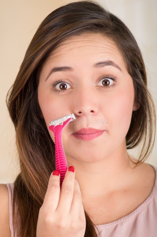 Ciérrese para arriba de una mujer joven hermosa que usa una máquina de afeitar que finge afeitar su bigote, en un fondo blanco imagen de archivo libre de regalías Ciérrese para arriba de una mujer joven hermosa que usa una máquina de afeitar que finge afeitar su bigote, en un fondo blanco imagen de archivo libre de regalías