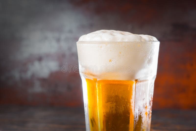 Ciérrese para arriba del vidrio con una cerveza ligera y un jefe grande de la espuma encendido fotos de archivo Ciérrese para arriba del vidrio con una cerveza ligera y un jefe grande de la espuma encendido fotos de archivo