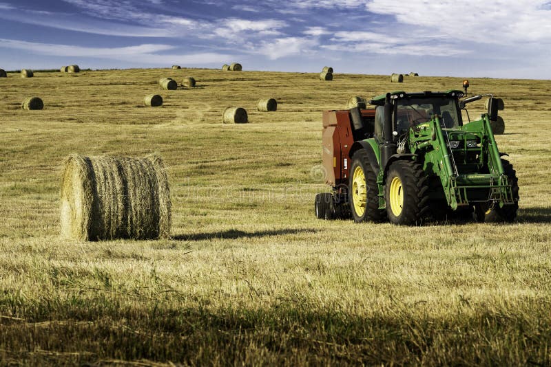 Rocky View County Alberta Canada,September 02 2022: A tractor pulling a baler baling round hay bales on a harvested field. Rocky View County Alberta Canada,September 02 2022: A tractor pulling a baler baling round hay bales on a harvested field.