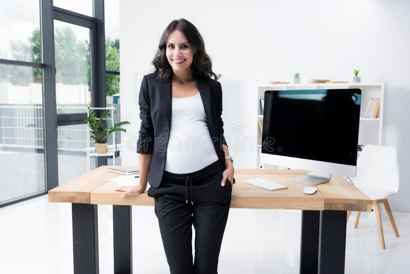 ciężarny bizneswoman oparty na worktable przy nowożytnym z powrotem zdjęcie stock ciężarny bizneswoman oparty na worktable przy nowożytnym z powrotem zdjęcie stock