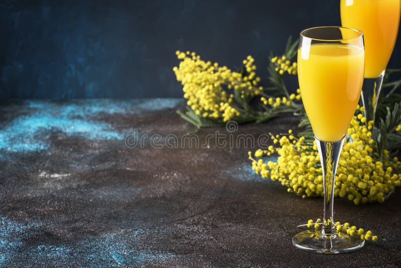 Classic alcohol cocktail mimosa with orange juice and cold dry champagne or sparkling wine in glasses, blue stone background with yellow flowers, copy space, spring mood, selective focus