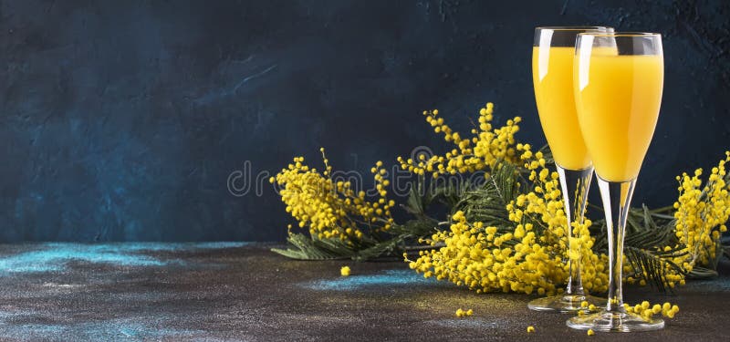 Classic alcohol cocktail mimosa with orange juice and cold dry champagne or sparkling wine in glasses, blue stone background with yellow flowers, copy space, spring mood, selective focus