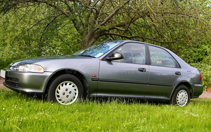 Classic dark silver sedan is parked on a grassy patch with trees and foliage in the background, the scene conveys a peaceful royalty free stock photo