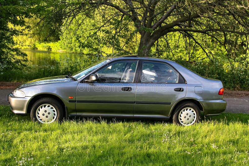 Classic dark silver sedan is parked on a grassy patch with trees and foliage in the background, the scene conveys a peaceful royalty free stock photography