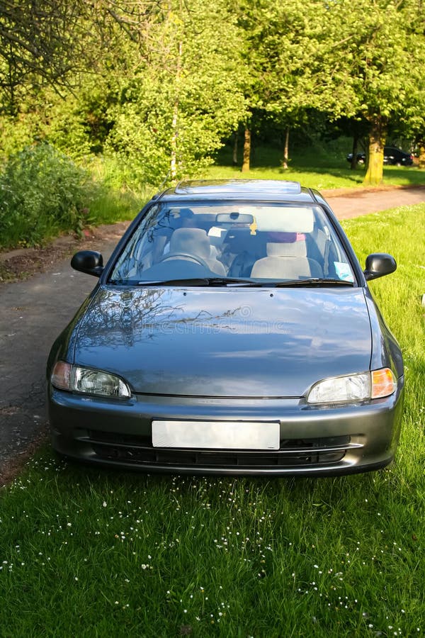 Classic dark silver sedan is parked on a grassy patch with trees and foliage in the background, the scene conveys a peaceful stock images