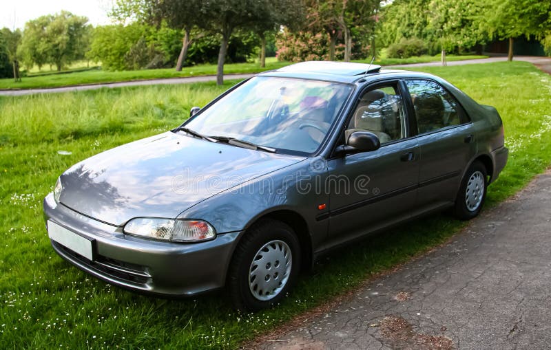 Classic dark silver sedan is parked on a grassy patch with trees and foliage in the background, the scene conveys a peaceful royalty free stock photos