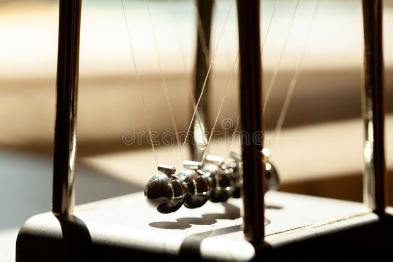 Classic Newtons cradle in sunlight, shallow dof, metal balls still macro, extreme closeup. Momentum, movement physics