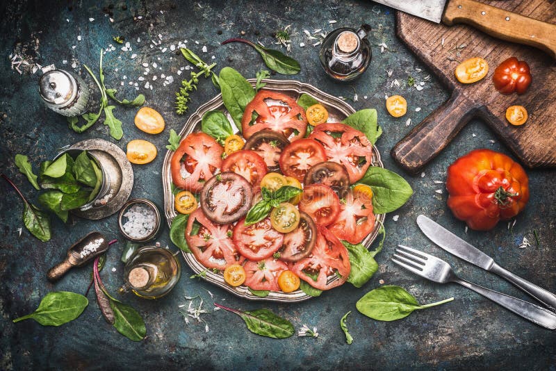 Classical traditional tomatoes mozzarella salad , preparation on dark rustic kitchen table with ingredients , cutting board and cu stock photography Classical traditional tomatoes mozzarella salad , preparation on dark rustic kitchen table with ingredients , cutting board and cu stock photography