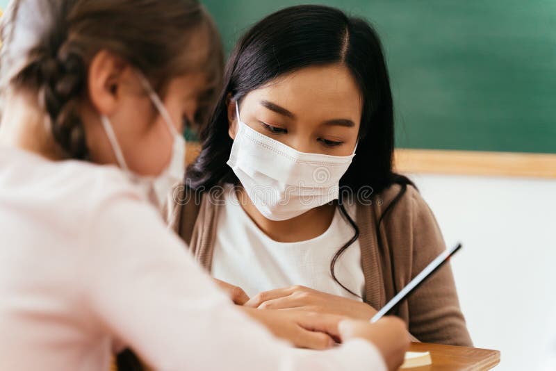 Clausura de profesora asiática con mascarilla en el edificio escolar que enseña a una estudiante de primaria. elemental imagen de archivo libre de regalías