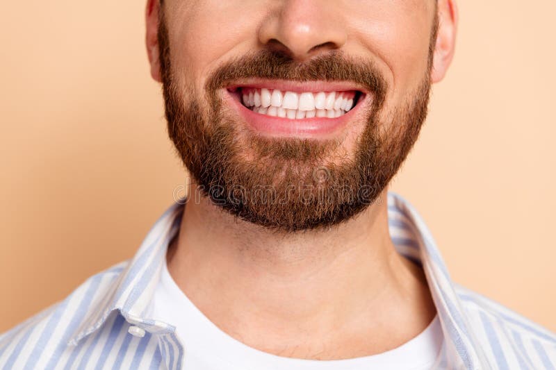 Clausura de un joven sonriente con una barba bien cuidada vestida con una camisa casual de rayas azules contra un beige fotografía de archivo