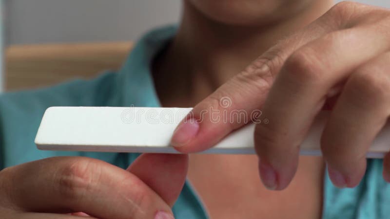 Clavos de la limadura de la mujer con el fichero de clavo durante el cierre casero de la manicura para arriba Mujer joven que hac