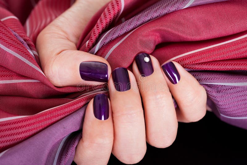 Woman with beautiful purple nails gripping a color matched maroon and purple fabric to show them off to best advantage. Woman with beautiful purple nails gripping a color matched maroon and purple fabric to show them off to best advantage