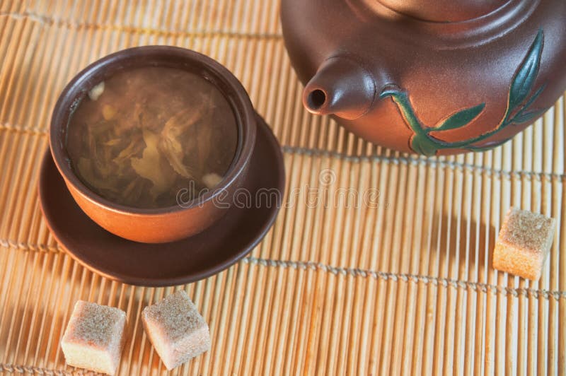 Clay cup and teapot with green tea and cane sugar cubes on a bamboo mat. Composition of a tea ceremony stock photography Clay cup and teapot with green tea and cane sugar cubes on a bamboo mat. Composition of a tea ceremony stock photography