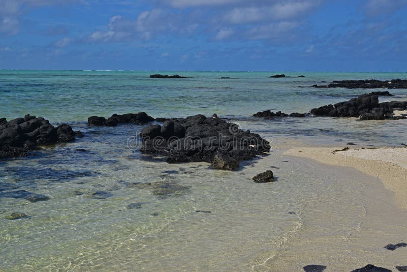 The clean clear transparent sea water off Ile aux Cerfs Mauritius with emerged black rocks and visible sandy beach