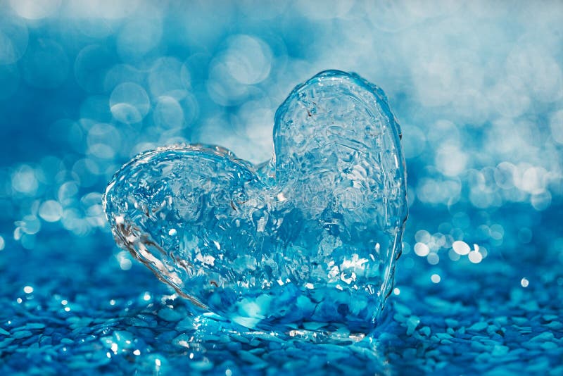 Clean glass heart on blue beach with water droplets