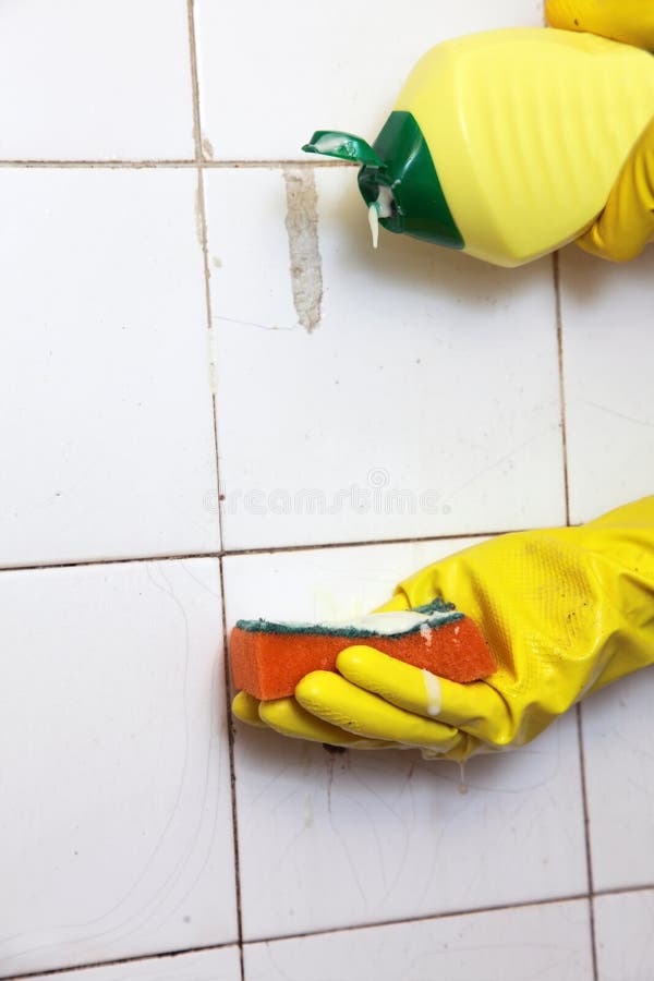 Gloved hand cleaning dirty old tiles with sponge in a bathroom. Gloved hand cleaning dirty old tiles with sponge in a bathroom