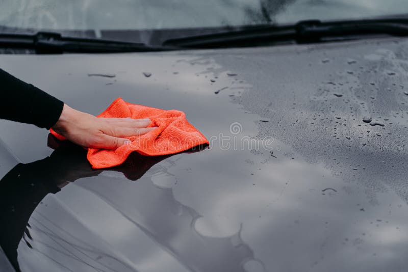 Cleaning car using microfiber cloth. Man washes black auto hood. Polishing vehicle. Car Detailing, maintenance