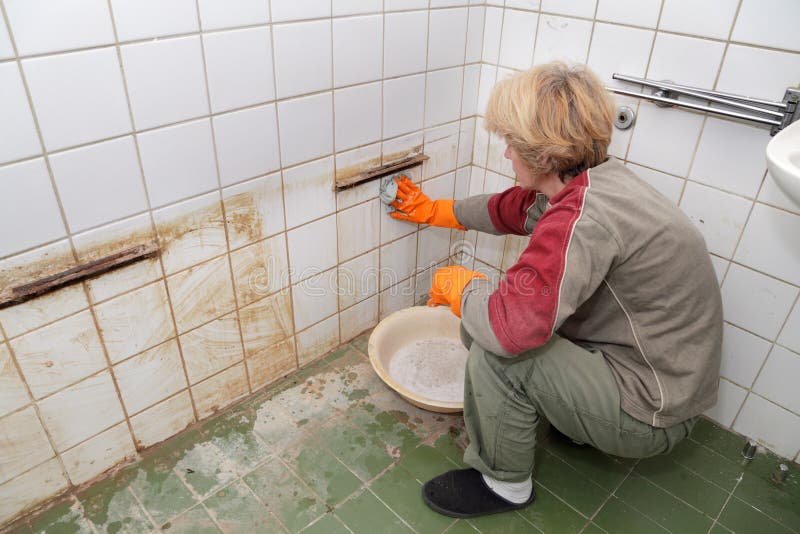 Middle age woman cleaning dirty old tiles in a bathroom. Middle age woman cleaning dirty old tiles in a bathroom