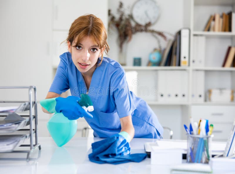 Cleaning Lady in Uniform Wipes Dust from Table in Office Stock Photo