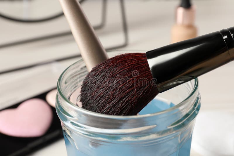 Cleaning Makeup Brushes in Jar with Special Liquid on White Table