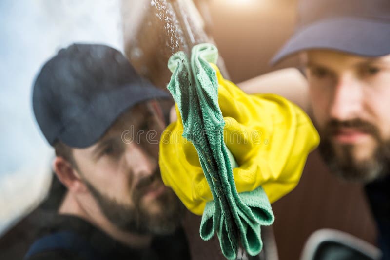 Cleaning service. Man in uniform and yellow gloves washes a car glass window in a car wash.