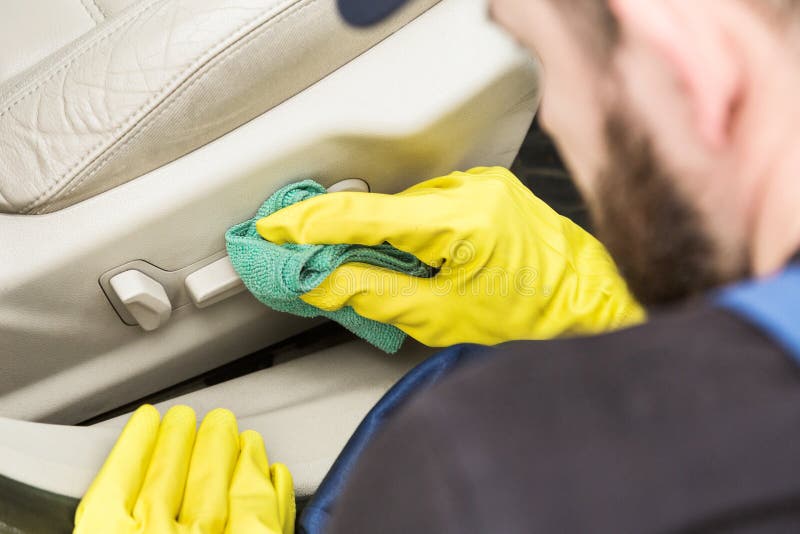 Cleaning service. Man in uniform and yellow gloves washes a car glass window in a car wash.