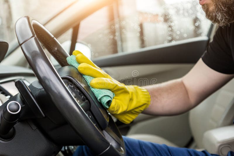 Cleaning service. Man in uniform and yellow gloves washes a car interior in a car wash.