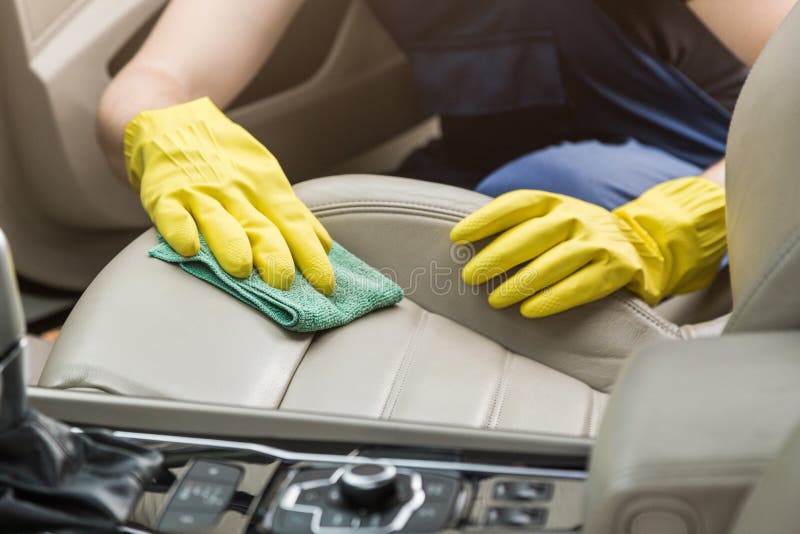 Cleaning service. Man in uniform and yellow gloves washes a car interior in a car wash. Worker washes the chairs of the leather salon.