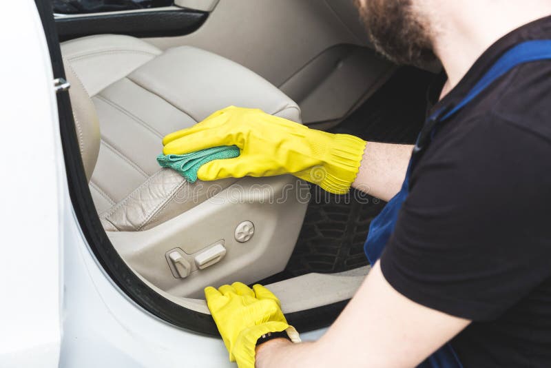 Cleaning service. Man in uniform and yellow gloves washes a car interior in a car wash. Worker washes the chairs of the leather salon.